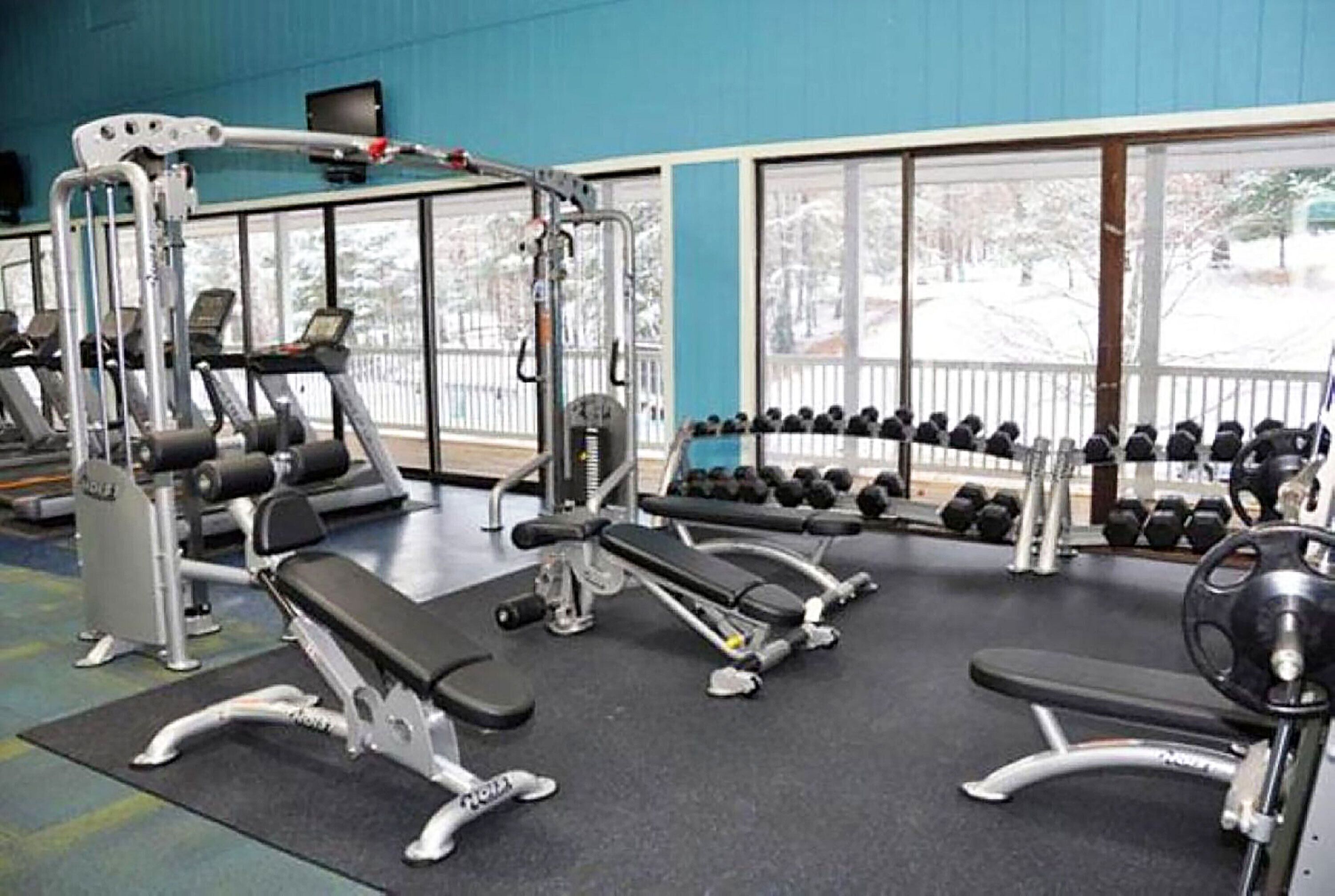 A gym with various exercise equipment, a bench, and dumbbells.