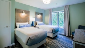 A hotel room with two beds, a desk, a chair, a window with curtains, and a ceiling light.