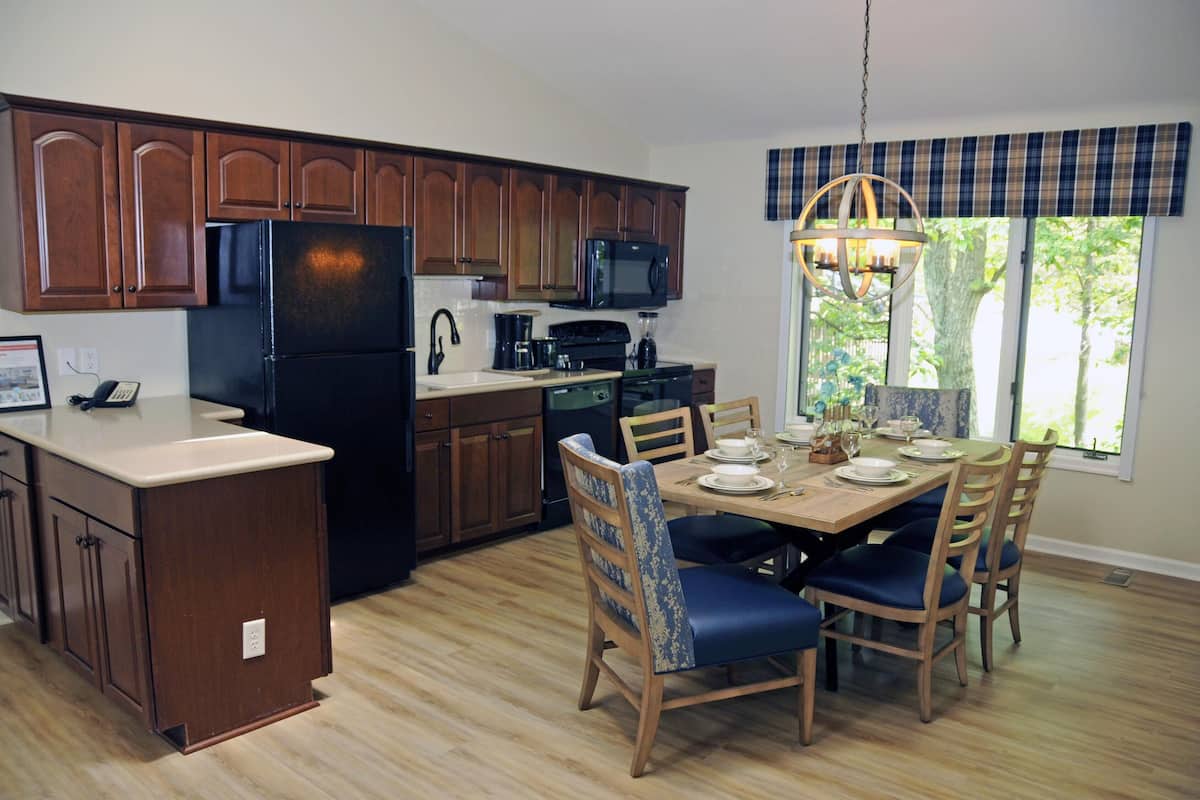 A kitchen with wooden cabinets, a black refrigerator, a microwave, and a dining table with chairs.