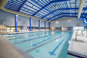 Una piscina interior con varias pistas de natación, sillones de descanso y un techo alto con vigas estructurales azules.