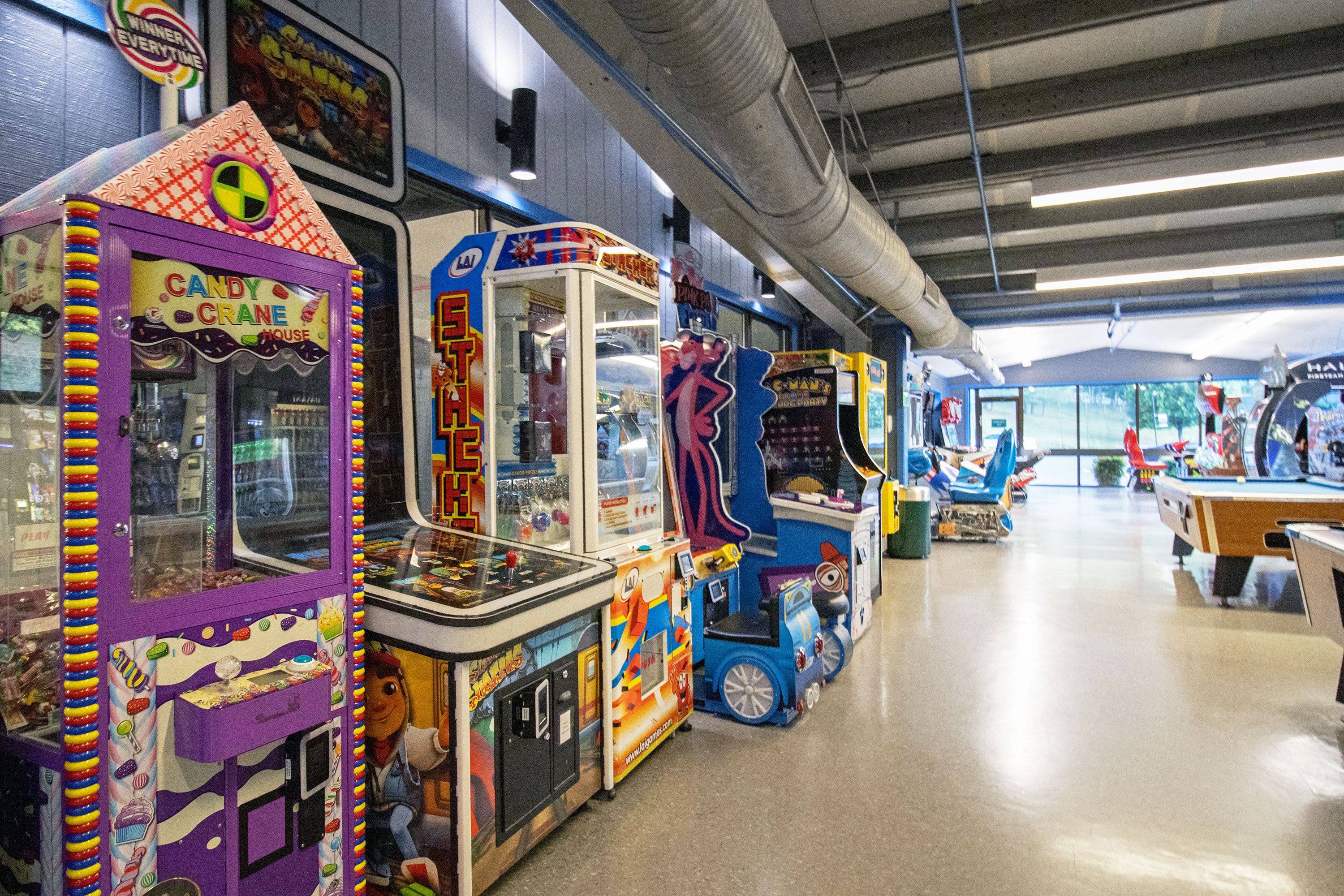 Una hilera de máquinas de arcade en un espacio interior bien iluminado con techo alto y conductos a la vista.