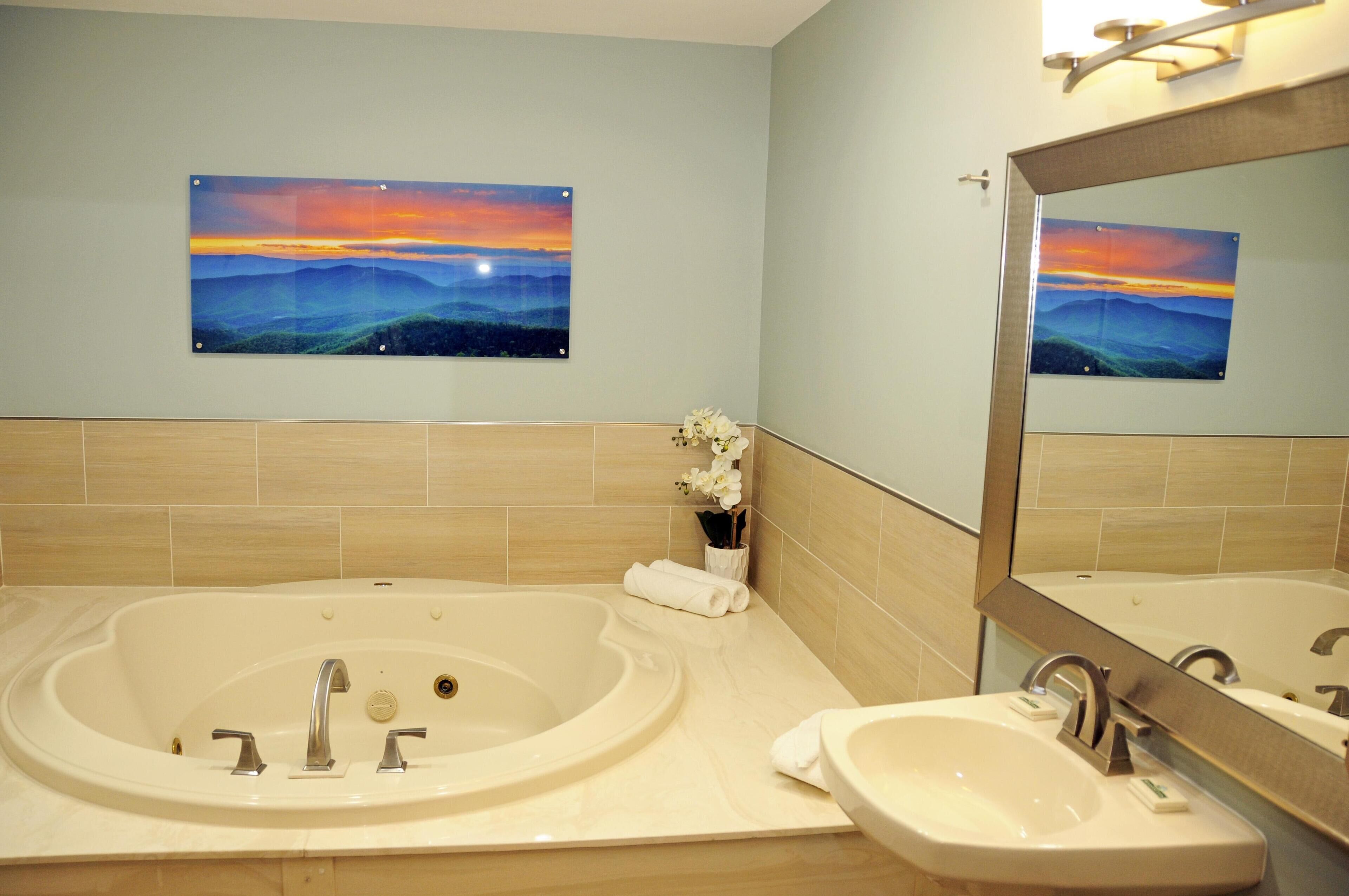 Un baño con una bañera grande, un lavamanos y dos cuadros del atardecer colgados en la pared.