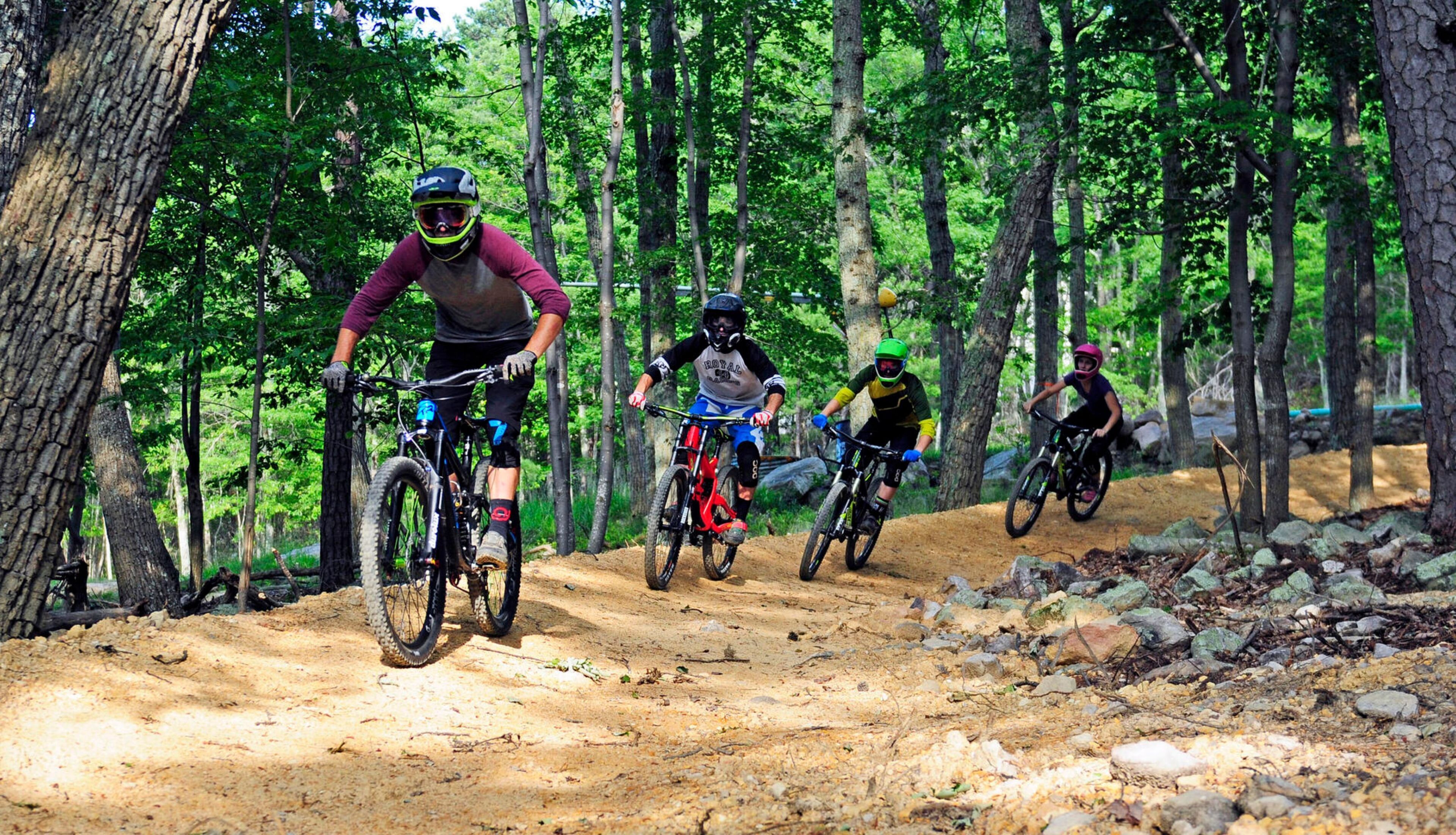 A group of mountain bikers on a dirt trail surrounded by trees.