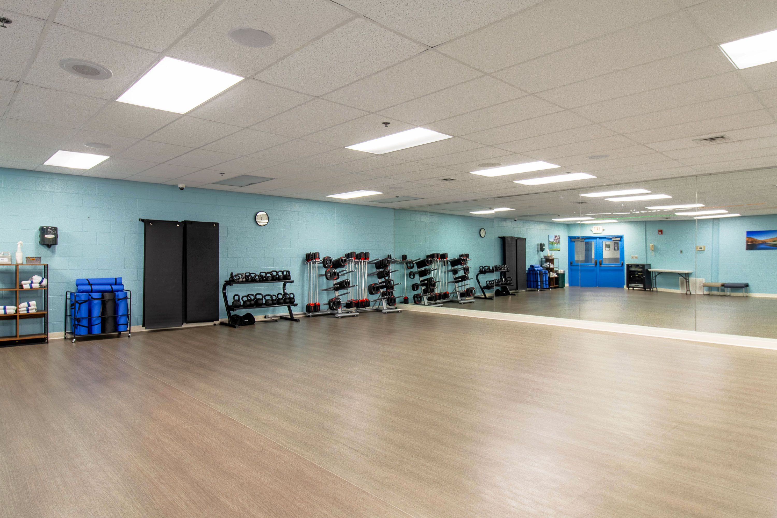 Un gimnasio amplio con equipo de levantamiento de pesas y una pared azul.