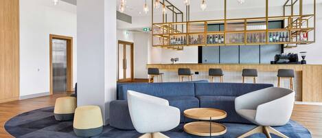 Un vestíbulo moderno con alfombra azul, dos sillones blancos, una mesa de centro de madera y una zona de bar con un expositor de vidrio.