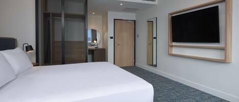 Een hotelkamer met een groot bed, een kledingkast, een spiegel, een televisie en een klein bureau met een lamp.