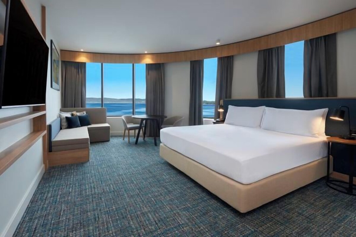 A hotel room with a large bed, a seating area with a view of the sea, and a flat-screen TV.