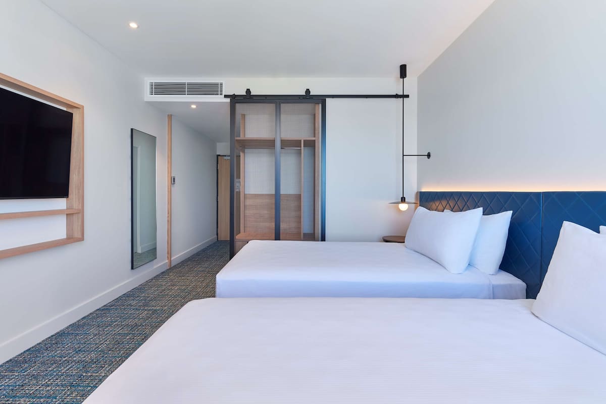 Ein Hotelzimmer mit zwei Betten, einem großen Fernseher, einem Schiebetürenschrank und einer wandmontierten Leuchte.