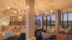 A modern hotel lobby with a bar area, seating arrangements, and large windows offering a view of the outdoors.