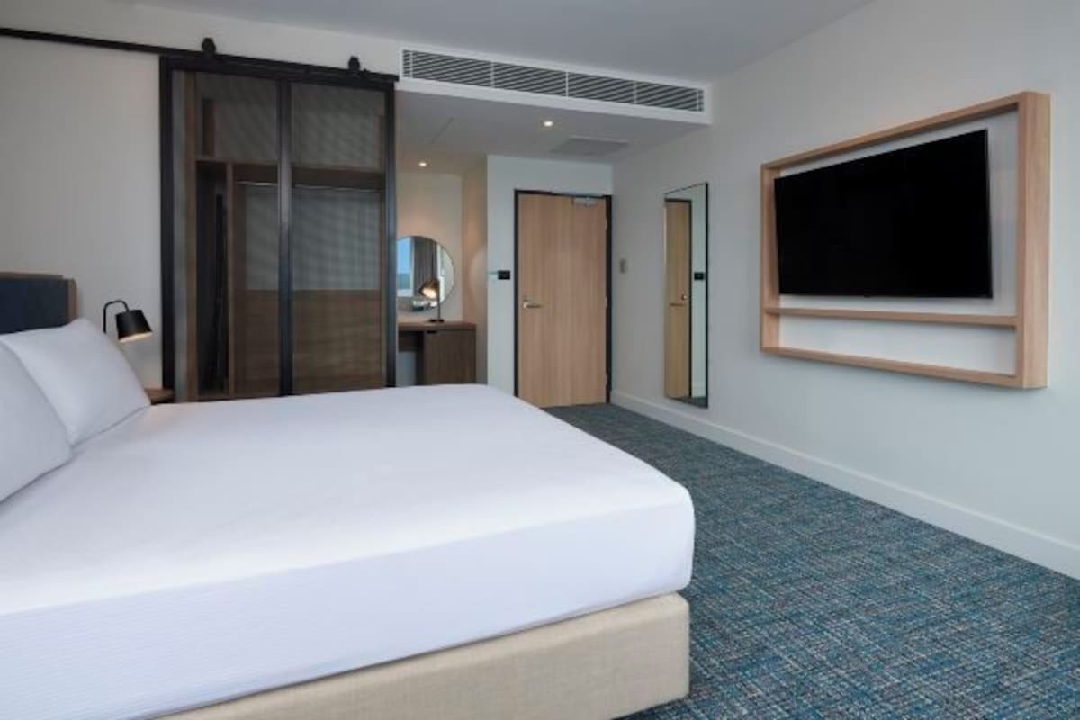 Une chambre d’hôtel avec un grand lit, un bureau avec une chaise, un miroir et un téléviseur fixé au mur.
