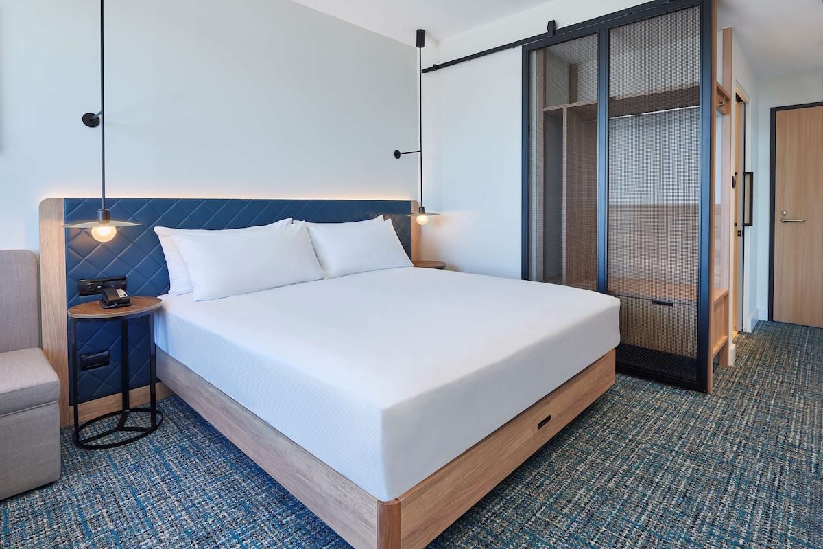 Ein modernes Hotelzimmer mit einem großen Bett, Nachttischen, einem Kleiderschrank und Teppichboden.