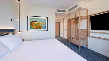 A hotel room with a large bed, a painting on the wall, a wardrobe, and a television.