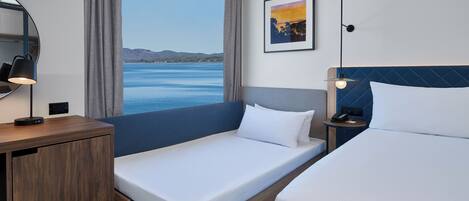 A hotel room with a large window, a bed, a desk, and a chair.