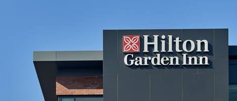 En skylt med texten ”Hilton Garden Inn” på fasaden av en modern byggnad.