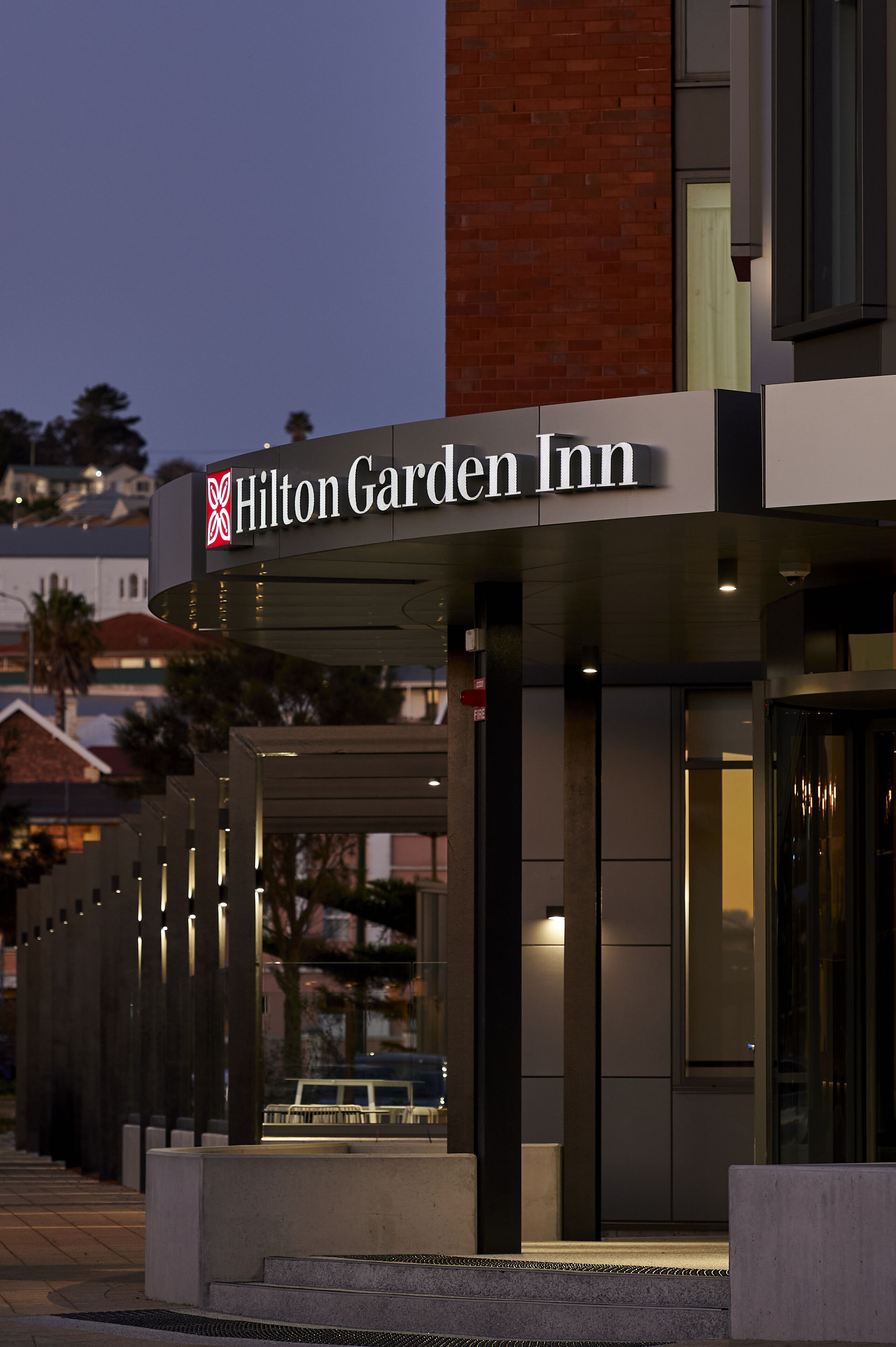 The exterior of the Hilton Garden Inn with a modern design, featuring a prominent sign and a well-lit entrance.