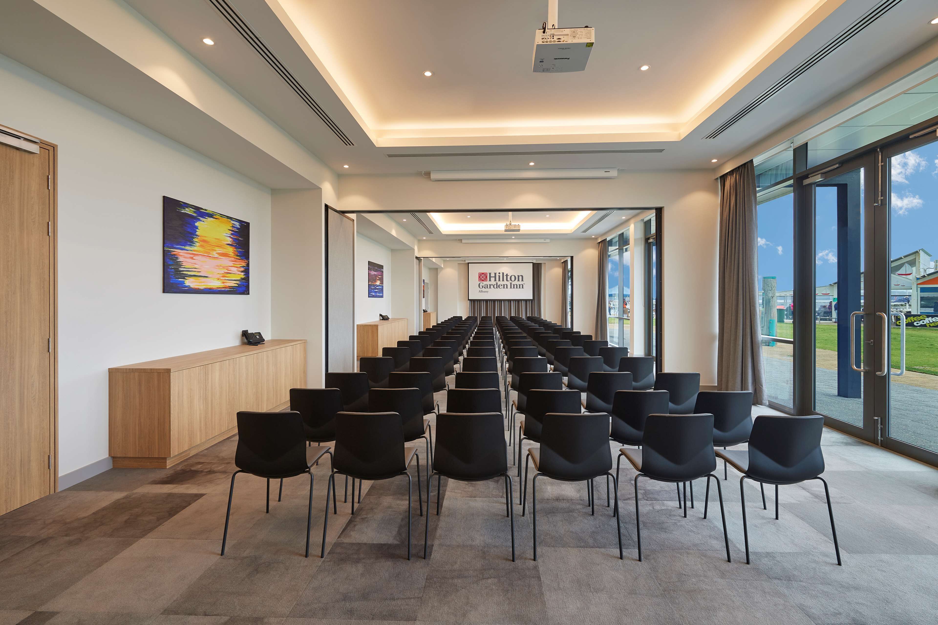 A conference room with rows of black chairs, a wooden reception desk, and a large window offering a view of the outside.