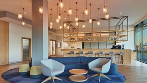 A modern lounge area with a sectional sofa, round coffee table, and ottomans. There is a bar area with stools and a glass display case.