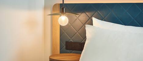 A neatly made bed with a wooden headboard, a bedside table, and a hanging light fixture.