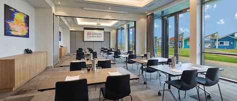 A conference room with tables and chairs, a projector screen, and a view of the outside.
