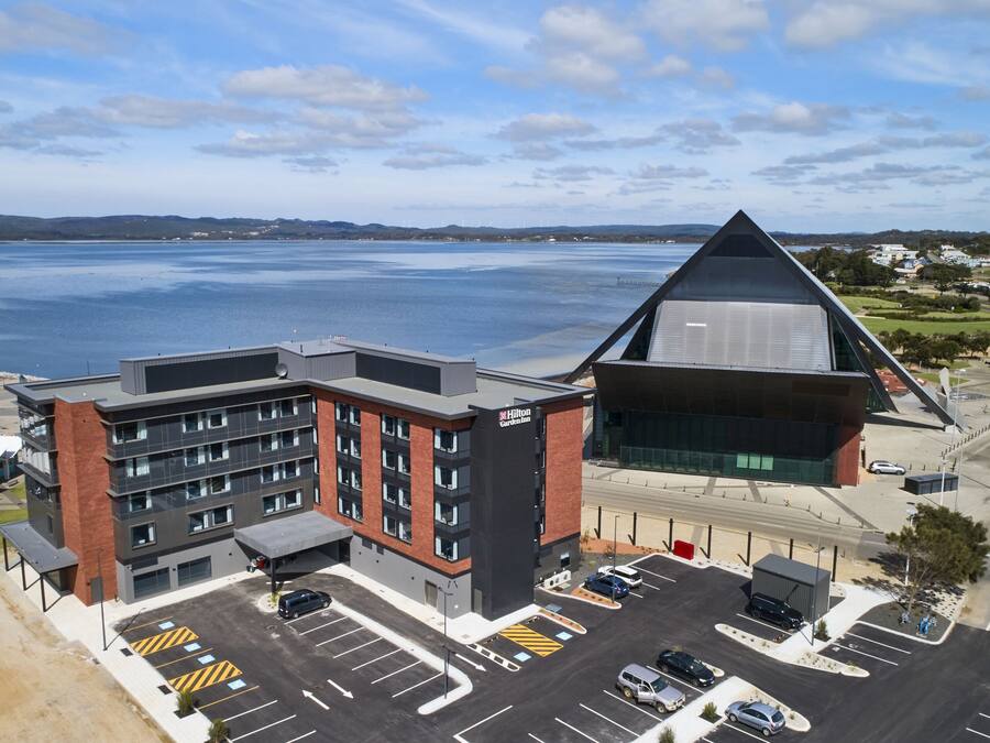 A modern hotel with a unique triangular roof, a parking lot, and a view of a body of water.