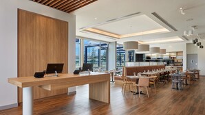 A modern restaurant with a wooden reception desk, large windows, and a variety of seating options.