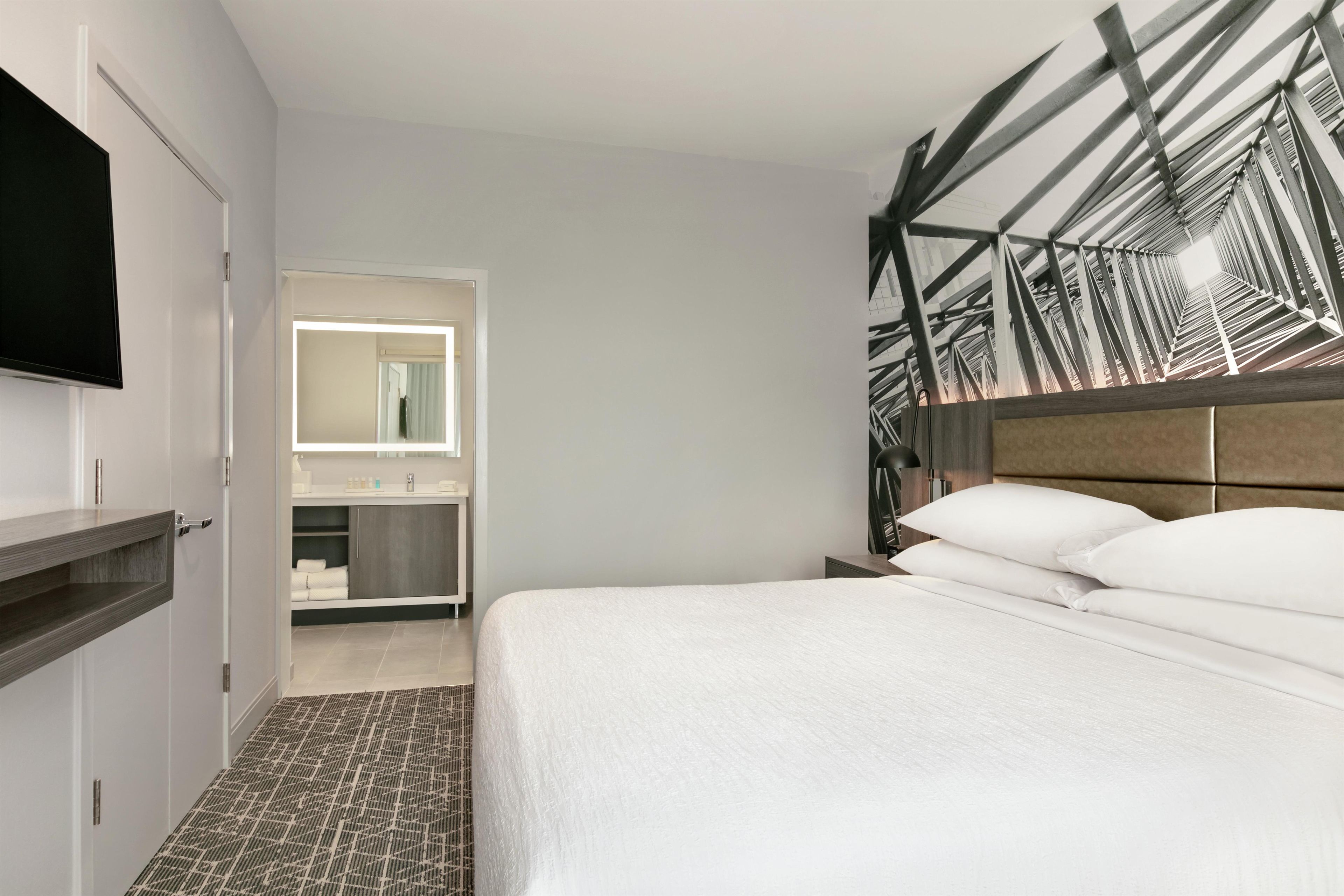 A hotel room with a bed, a television, a mirror, and a bathroom.