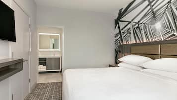 A hotel room with a bed, a television, a mirror, and a bathroom.