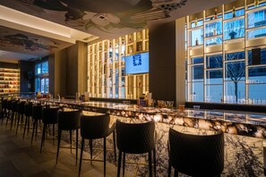 A bar area with a marble countertop, black cushioned bar stools, a television screen, and shelves with bottles. - Embassy Suites by Hilton Atlanta Midtown (Atlanta)