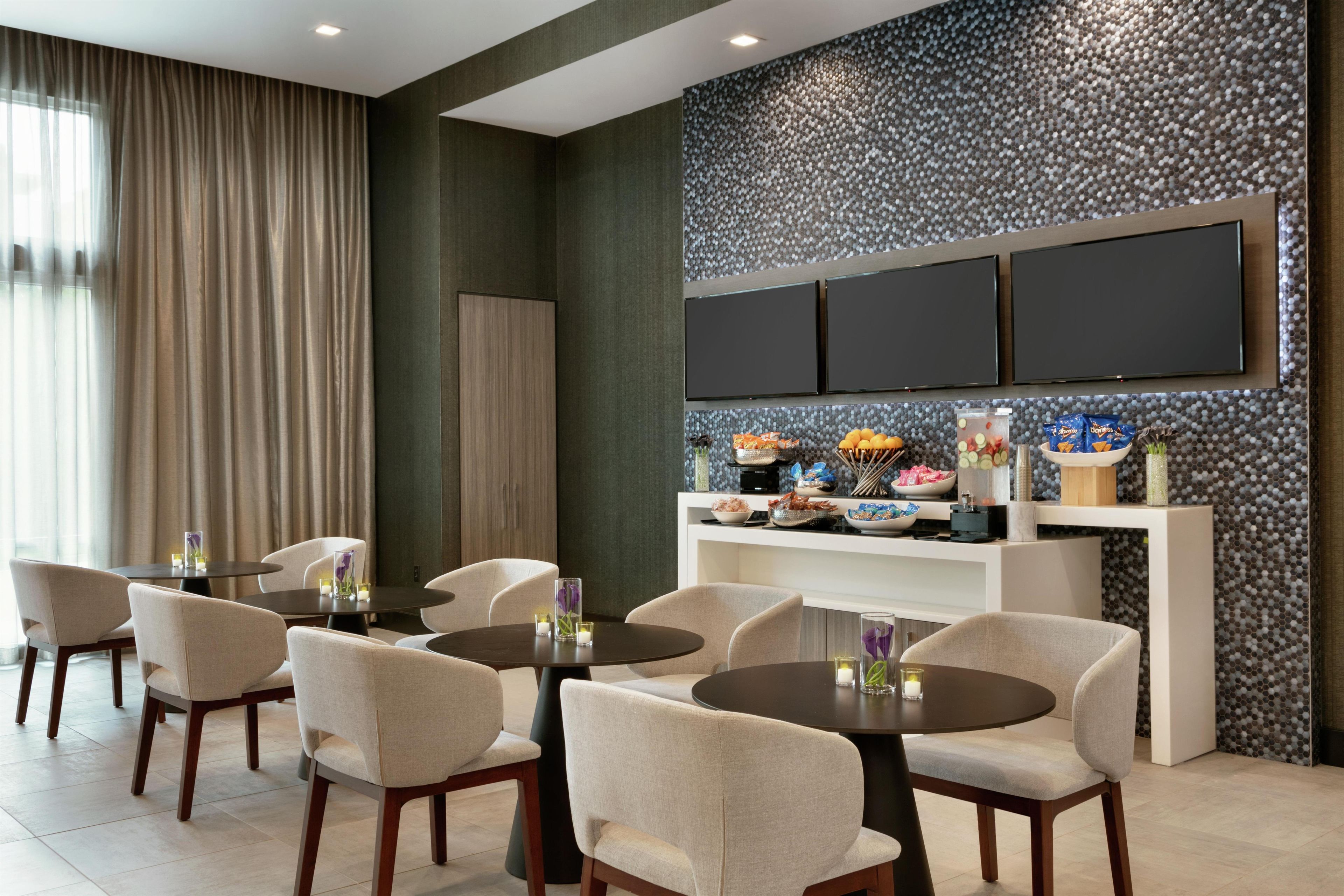 A hotel dining area with round tables, chairs, and a wall-mounted TV.