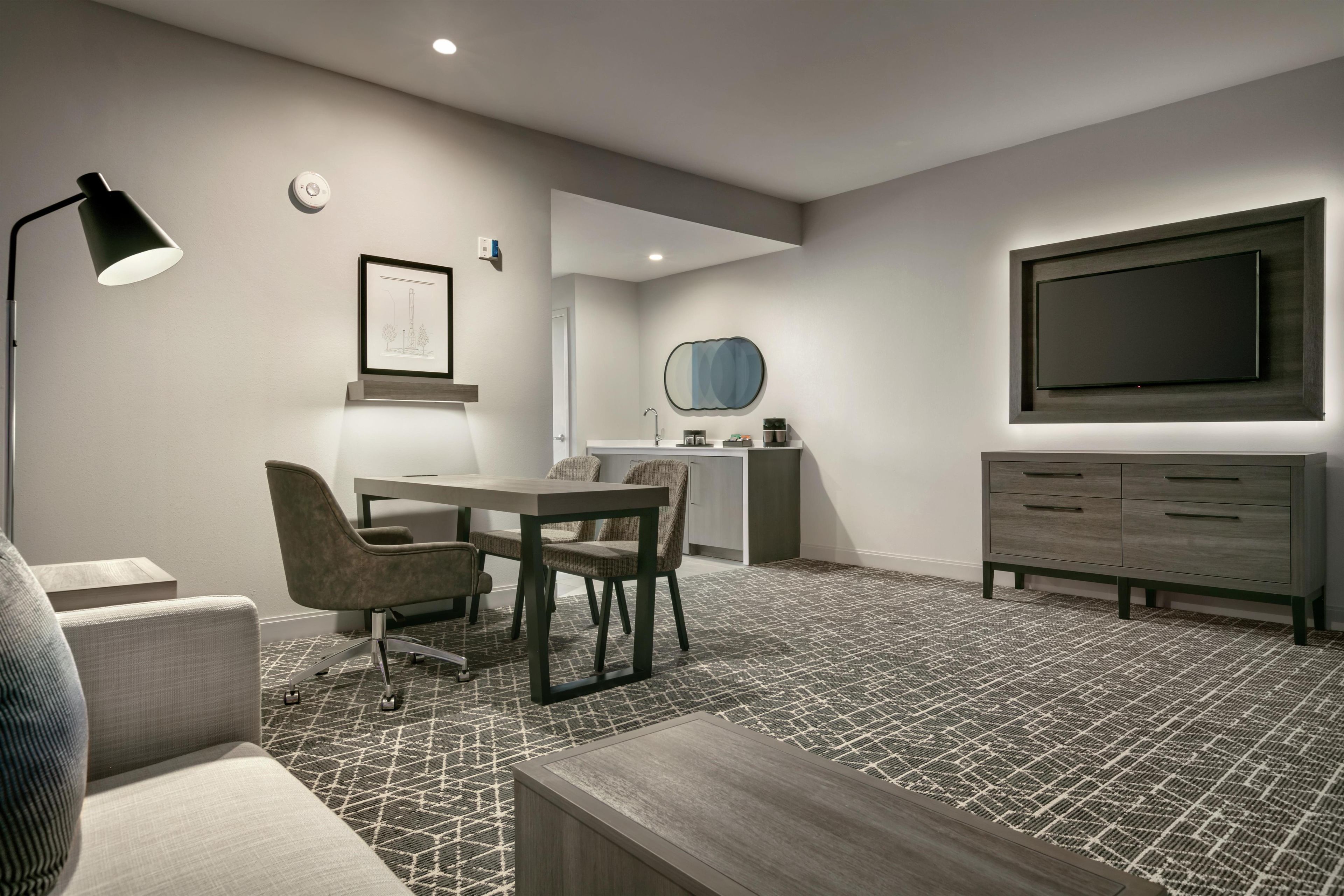 Una habitación de hotel moderna con zona de comedor, televisor de pantalla plana, escritorio y sofá.