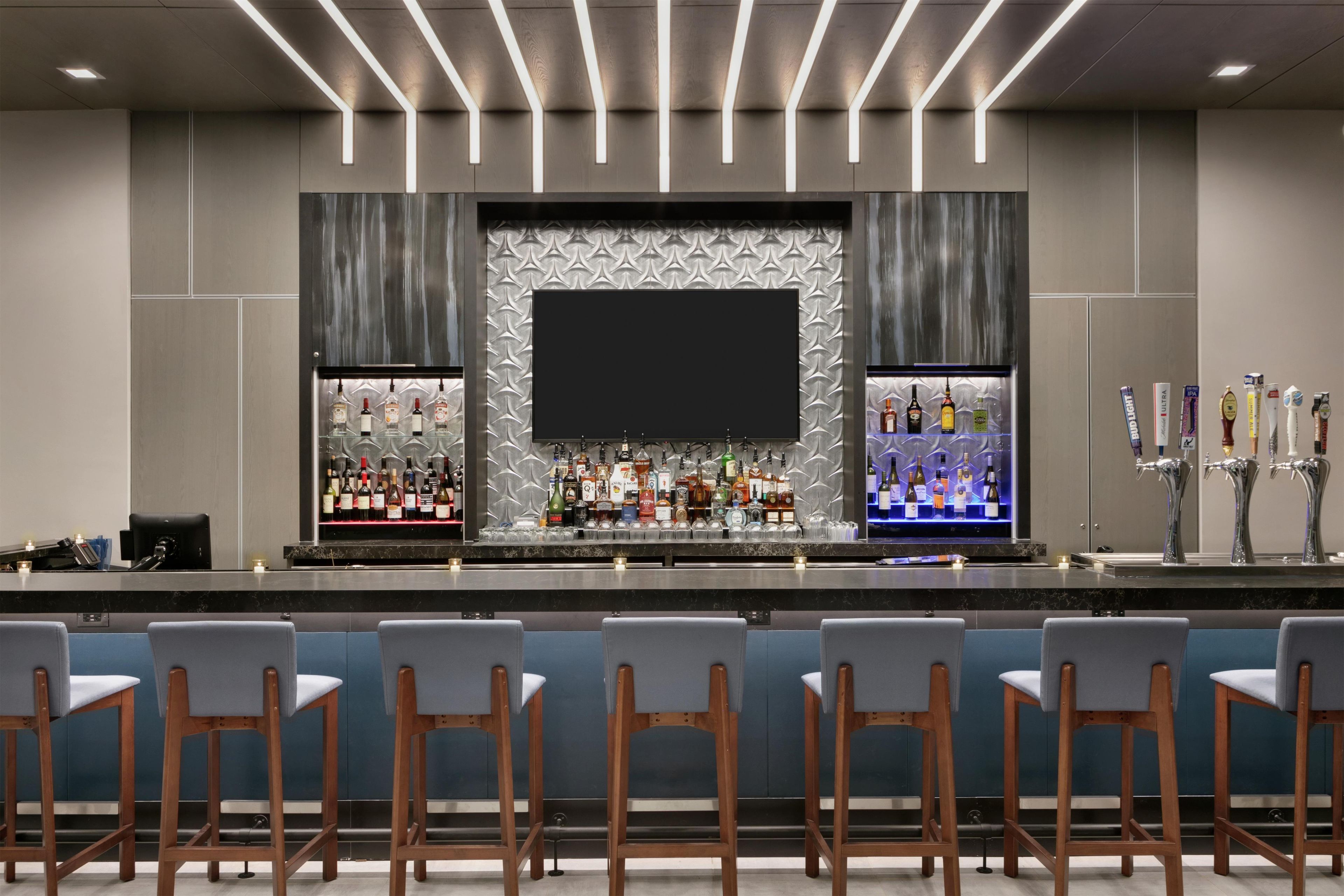 A bar area with a flat-screen TV, shelves of liquor bottles, and a bar counter.