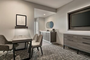A modern hotel room with a dining area, a large flat-screen TV, a framed artwork, and a patterned carpet. - Embassy Suites by Hilton Atlanta Midtown (Atlanta)