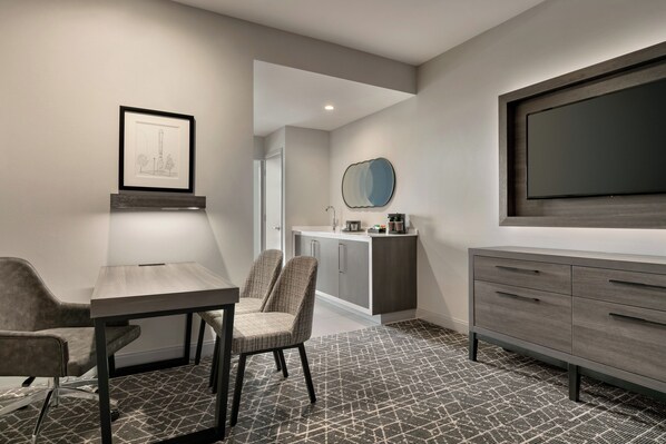 A modern hotel room with a dining area, a large flat-screen TV, a framed artwork, and a patterned carpet. - Embassy Suites by Hilton Atlanta Midtown (Atlanta)
