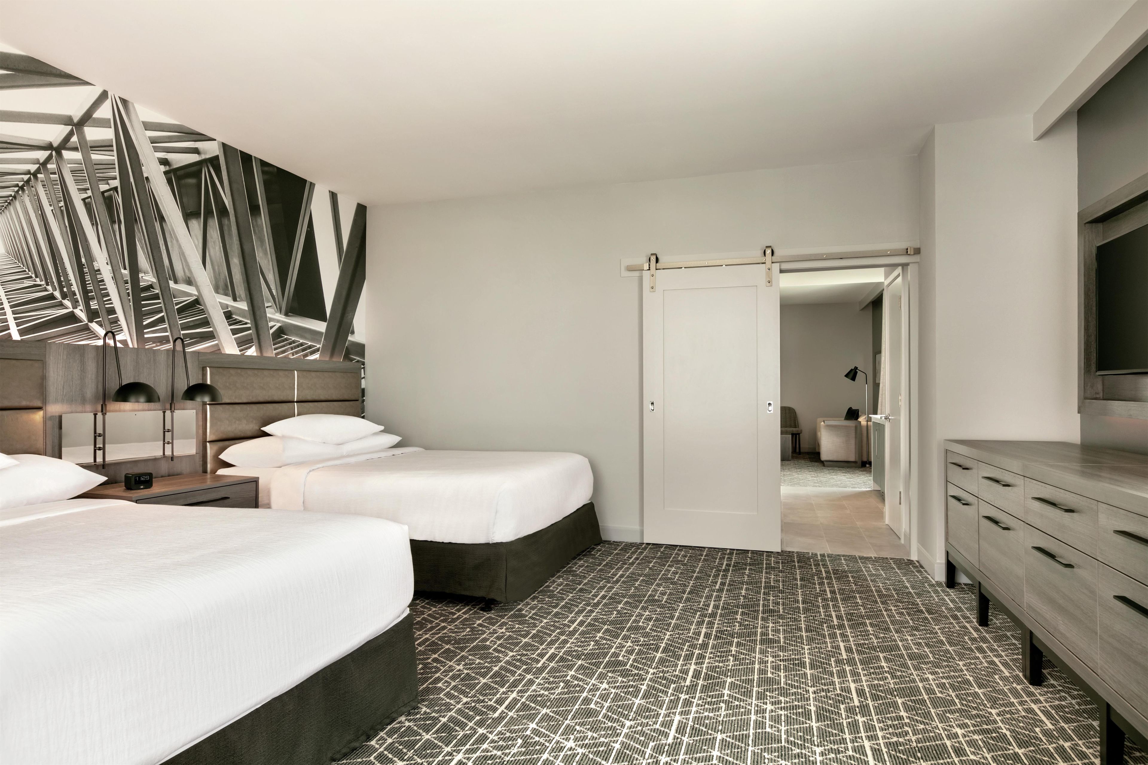 Une chambre d’hôtel moderne avec deux lits, un grand miroir, une armoire et une vue sur la salle de bain.