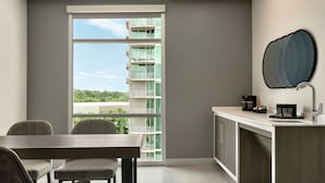 A modern kitchen with a large window, a dining area with wicker chairs, and a view of a building with balconies. - Embassy Suites by Hilton Atlanta Midtown (Atlanta)