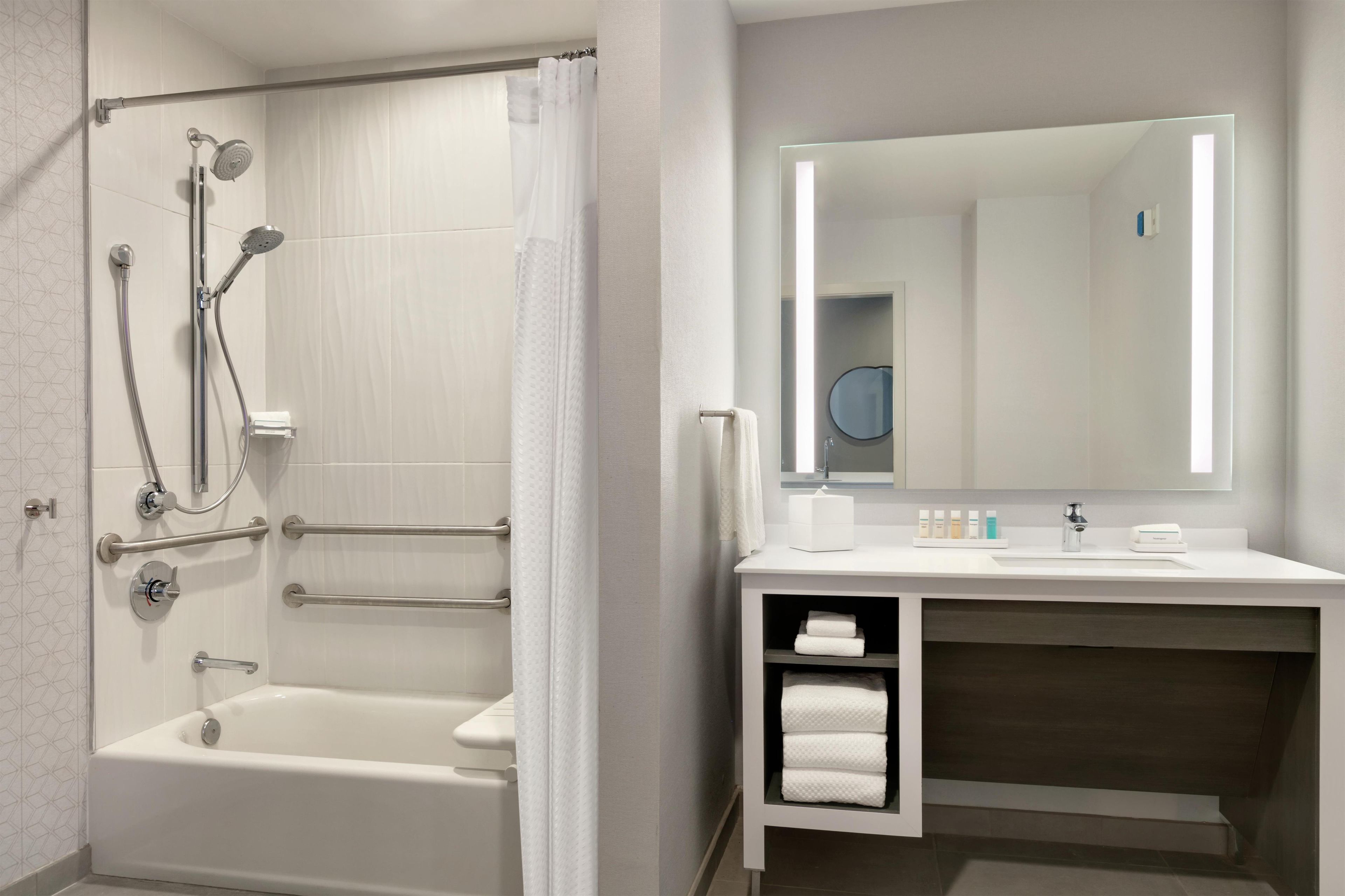 A modern bathroom with a walk-in shower, a bathtub, a vanity with a mirror, and a towel rack.