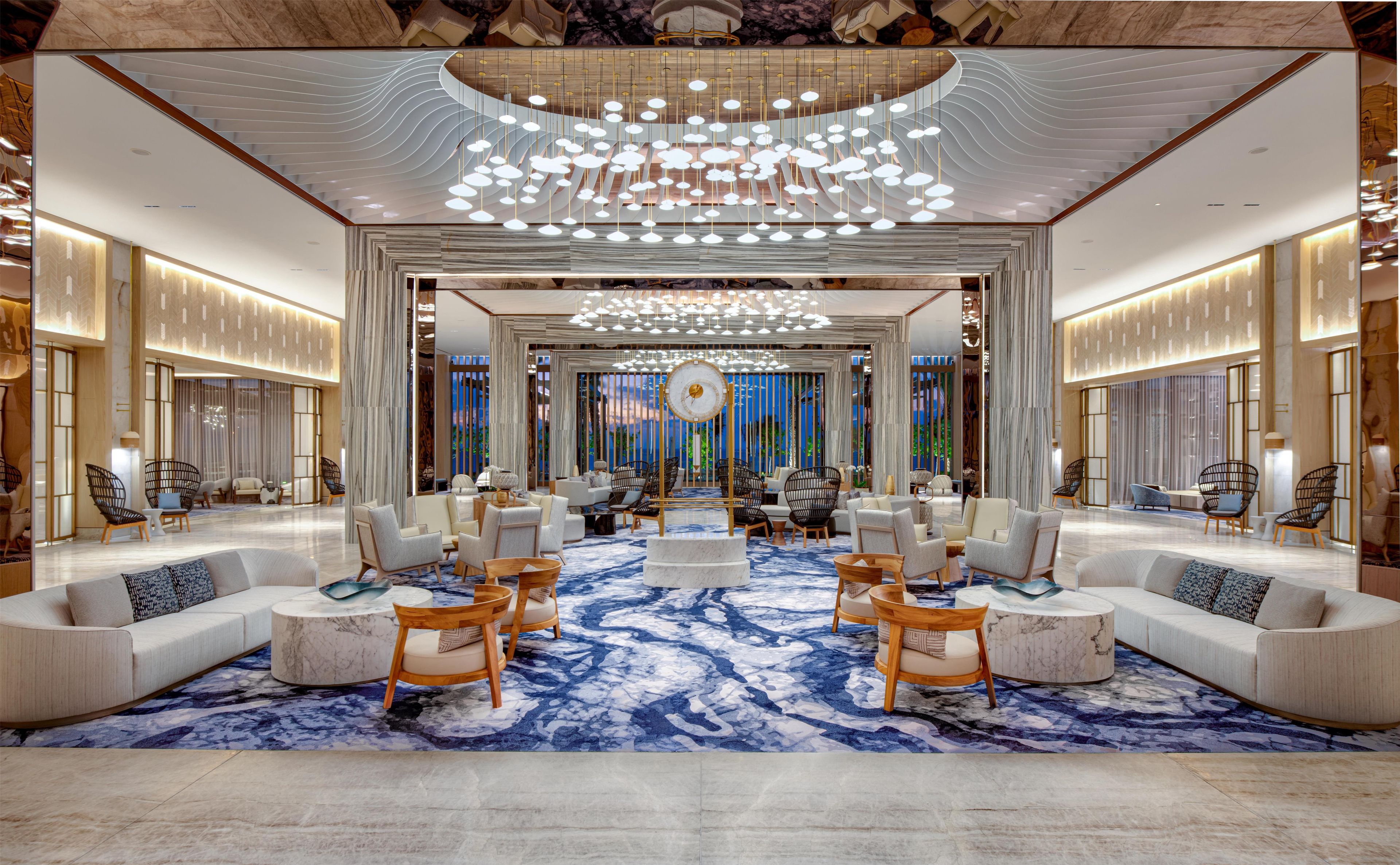 A spacious lobby with a central seating area, a large chandelier, and a view through a glass partition.