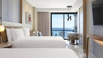 Ein Hotelzimmer mit zwei Betten, einem Balkon mit Blick und einem Essbereich mit Stühlen.