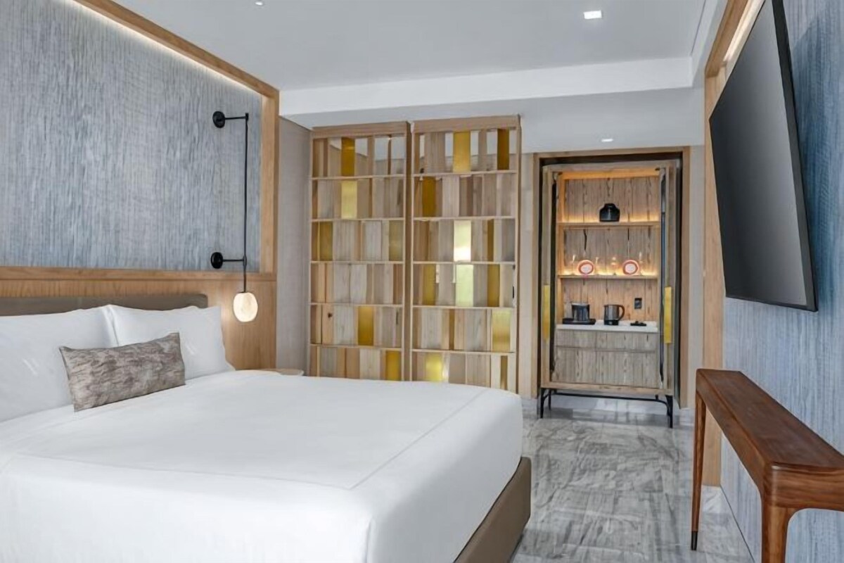 A hotel room with a large bed, a TV, a wooden wardrobe, and a small table.