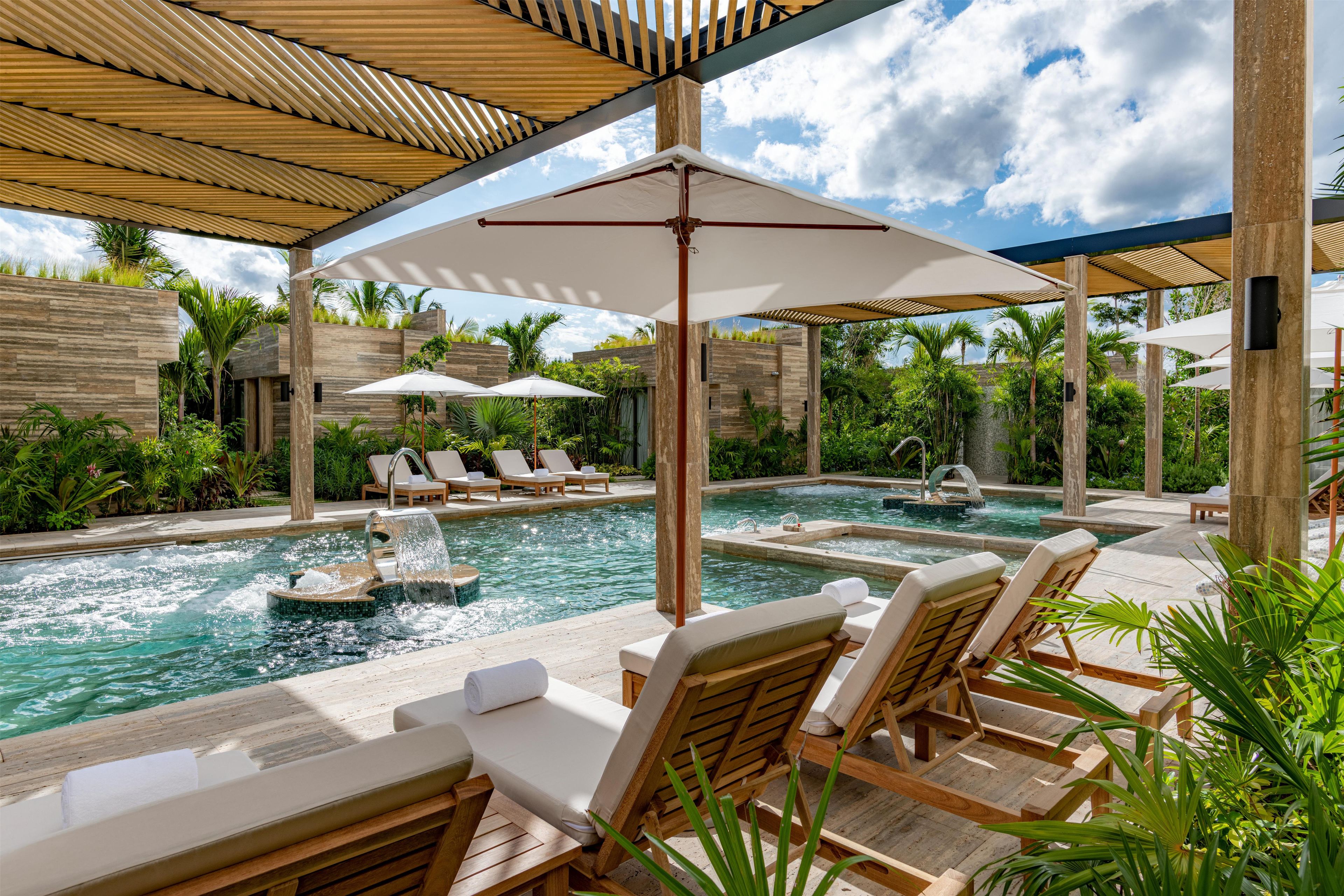 A pool area with lounge chairs, a water feature, and a covered seating area.
