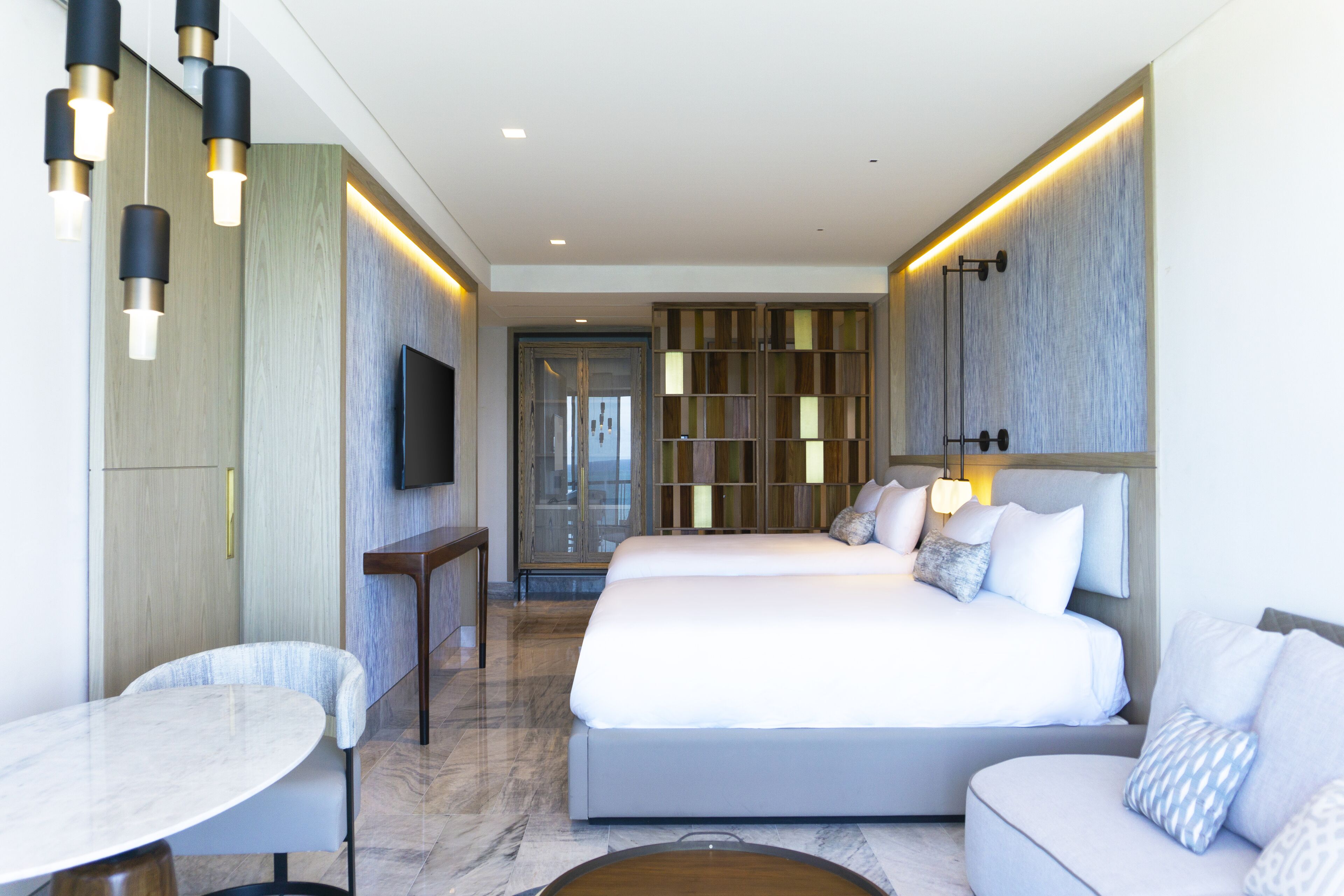 A modern hotel room with a large bed, a TV, a small table, and a sofa.