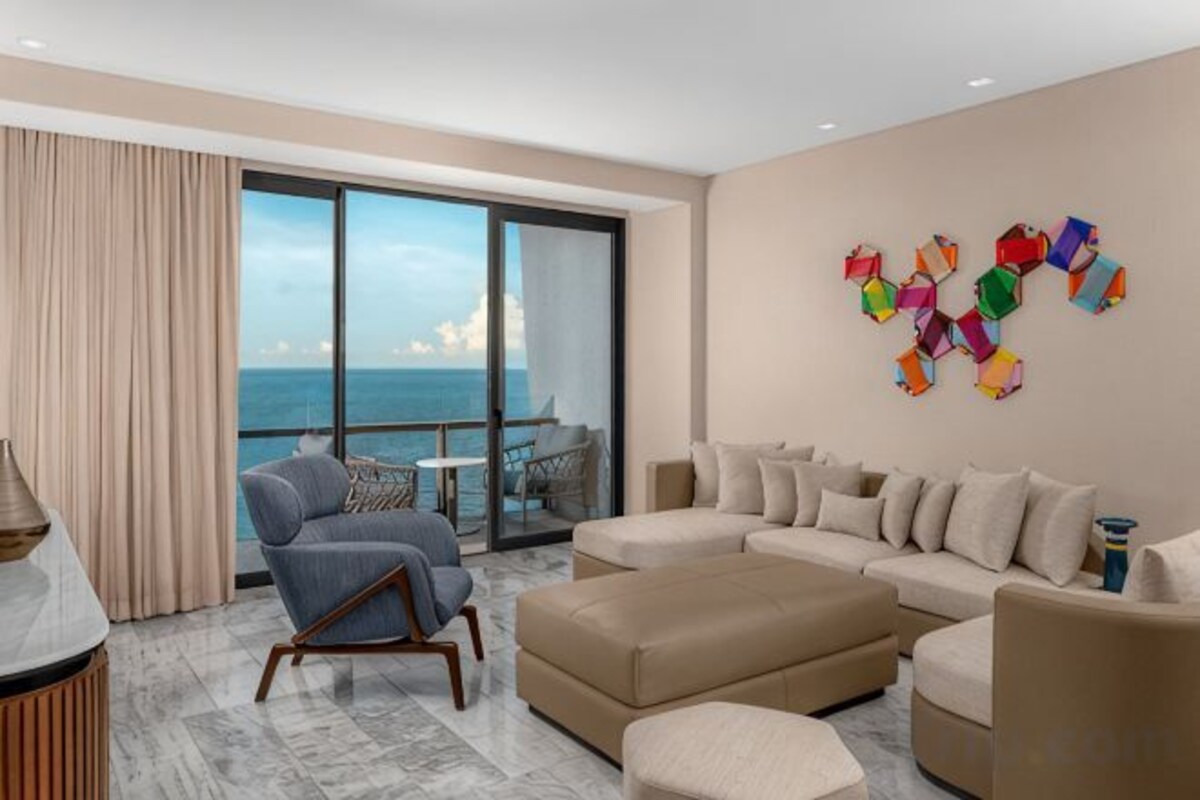 A modern living room with a large window, a sofa set, and a decorative wall piece.