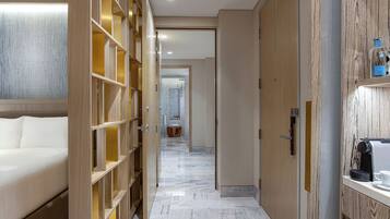 Un couloir d’hôtel avec un lit, des étagères en bois, une machine à café et, au fond, une salle de bain.