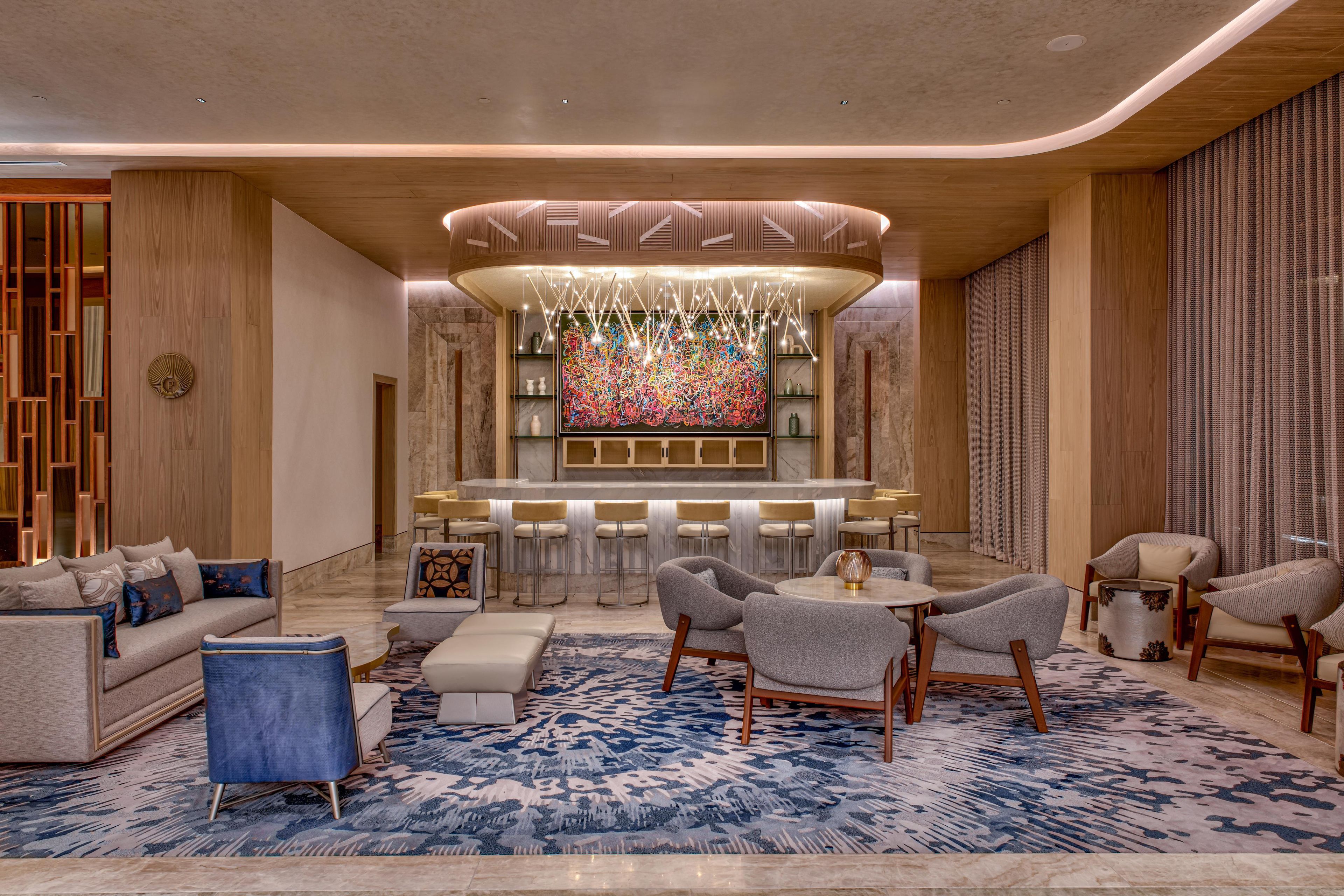 A modern lobby with a bar area, seating arrangements, and a large abstract art piece.