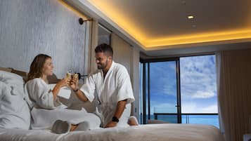 Una pareja en una habitación de hotel con una cama grande, vista al mar y un diseño interior moderno.