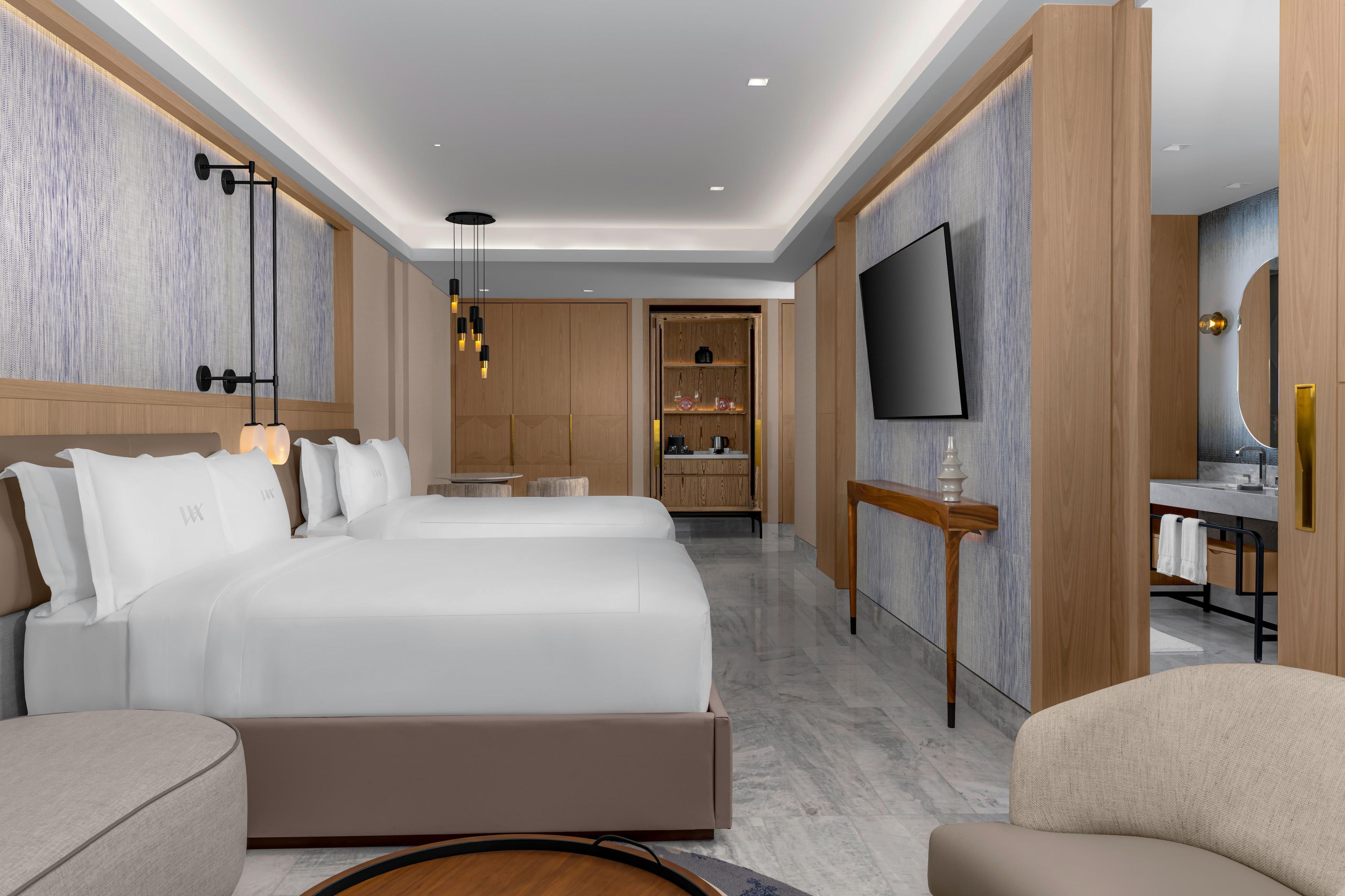 A modern hotel room with a large bed, a TV, a desk, and a bathroom visible through an open door.