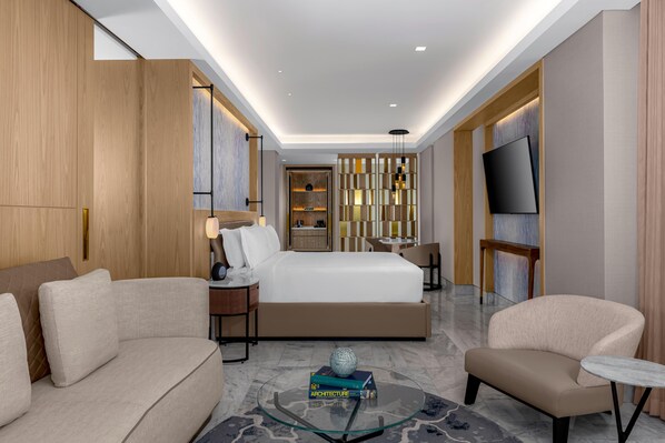 A modern hotel room with a bed, a sofa, a chair, a small table, a TV, and a decorative wall panel. - Waldorf Astoria Riviera Maya, an All-Inclusive Experience (Cancun)