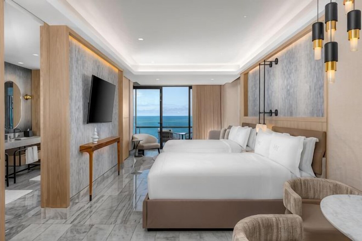 A modern hotel room with a large bed, a TV, a balcony with a view, and a desk with a chair.