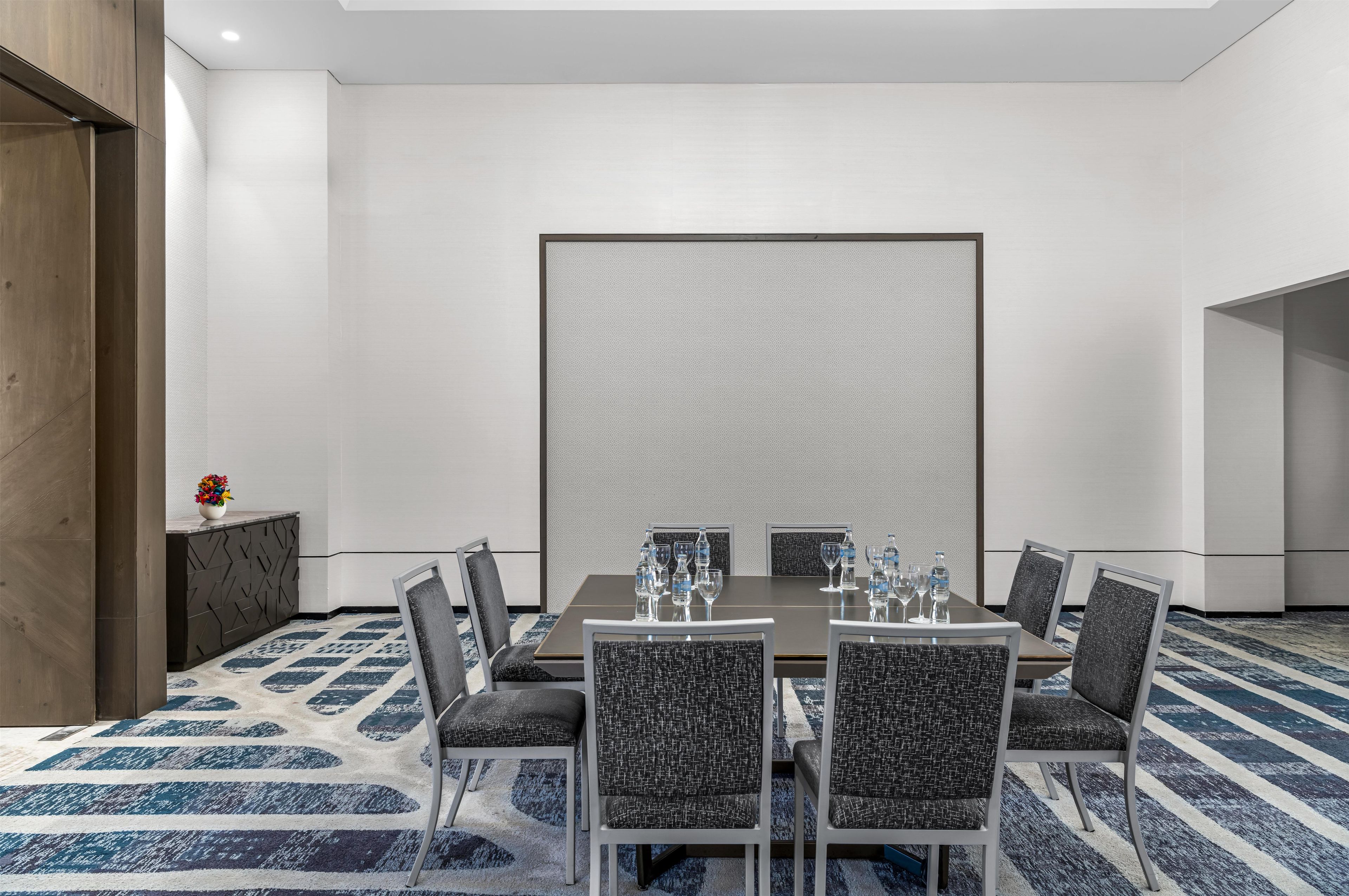 A conference room with a large table, six chairs, and a decorative rug.