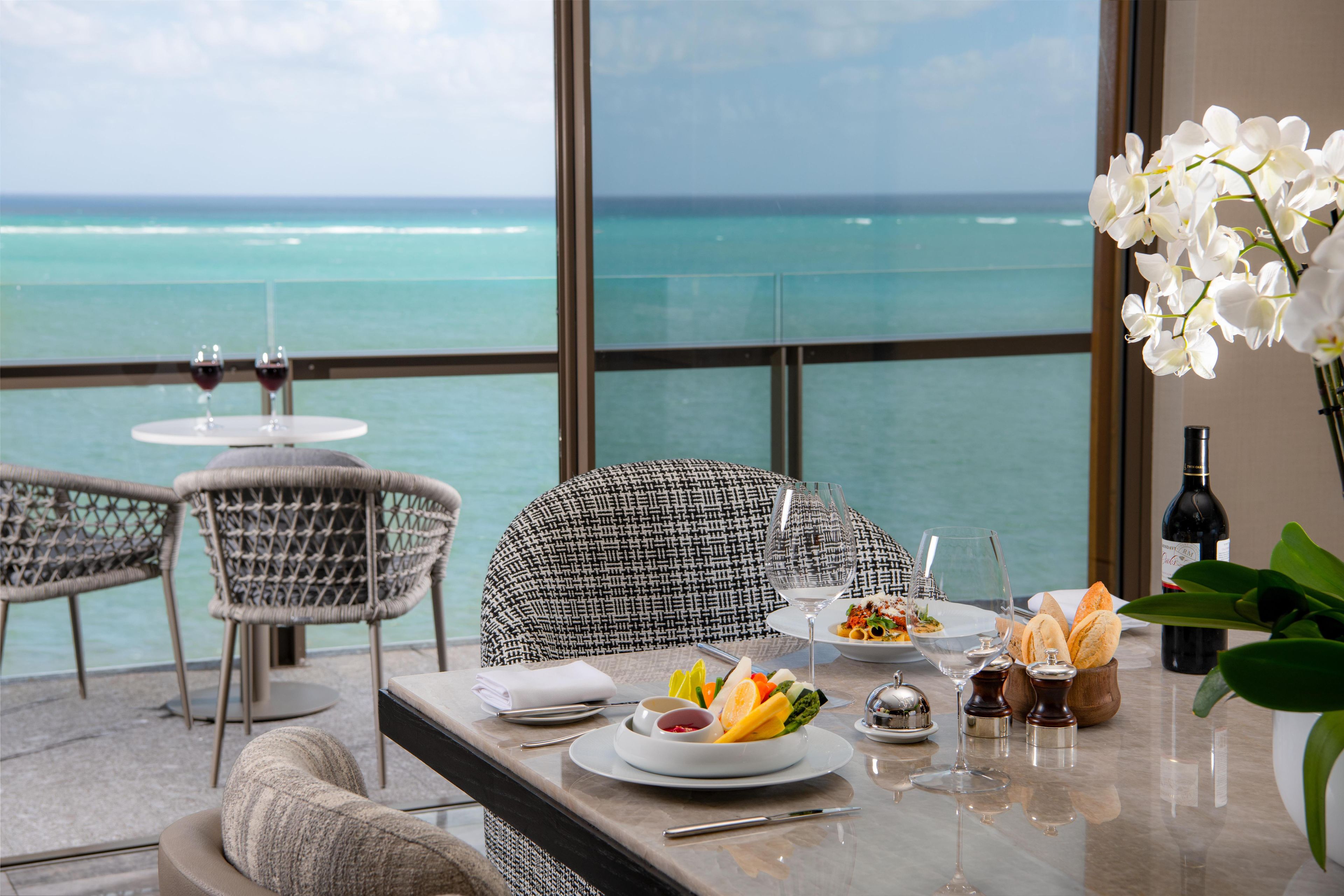 A dining area with a view of the ocean, featuring a table set with plates, glasses, and a bottle of wine.